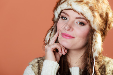 在演播室的橙色背景上穿着毛皮冬冠帽的时髦漂亮女人肖像图片