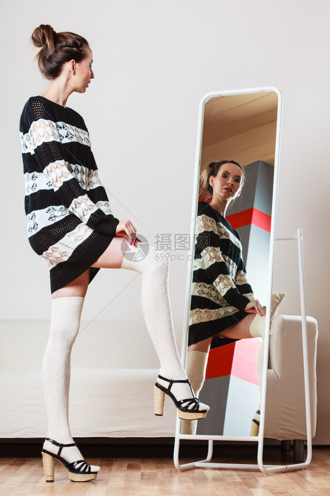 时装和购物穿着毛衣的女人选择服迷的女沙子看着镜站在服装店里图片