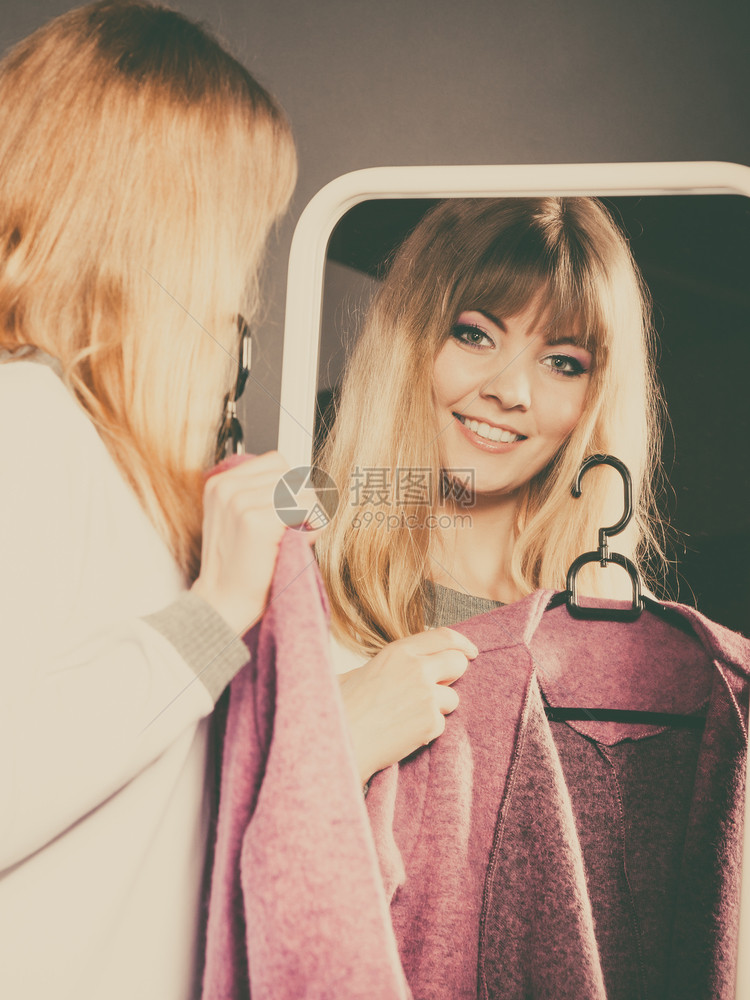 漂亮的女人看着她穿新衣柜的物照着镜子看年轻不决断的女沙巴二手选择购物概念图片