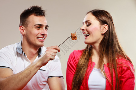 微笑的男人用蛋糕喂快乐的女人妻子和丈夫吃热量食品图片