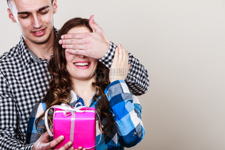 微笑的年轻男人令惊讶的快乐女带着礼物盒亲手遮住她的眼睛图片