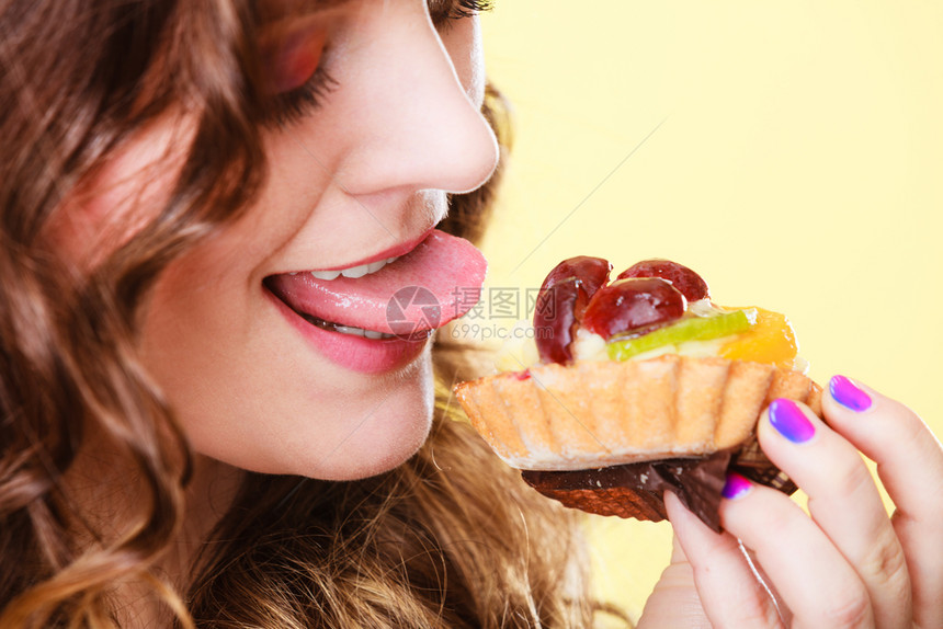 甜和快乐的概念可爱的女人吃水果蛋糕玩得开心的舌头脸部形象黄色背景图片
