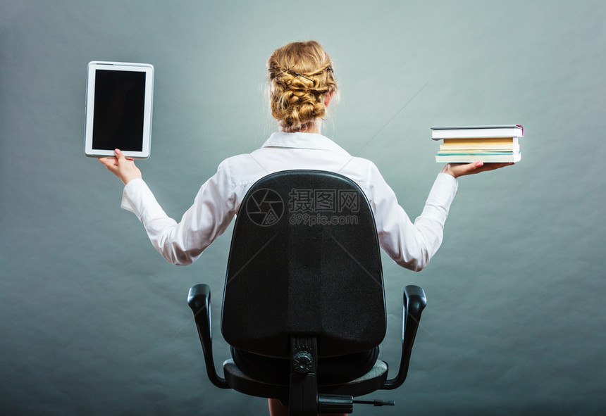 Ebookvsbook坐在椅子上持有传统书籍和电子阅读器平板电脑的女士背对视图粗景图片
