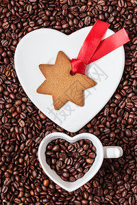 圣诞时间概念姜饼干明星在碟子上塑造白色杯子在咖啡豆背景上的心脏形状图片