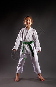一个女孩在传统的白色和服中用空手道和绿带在黑暗背景下开展训练演习图片