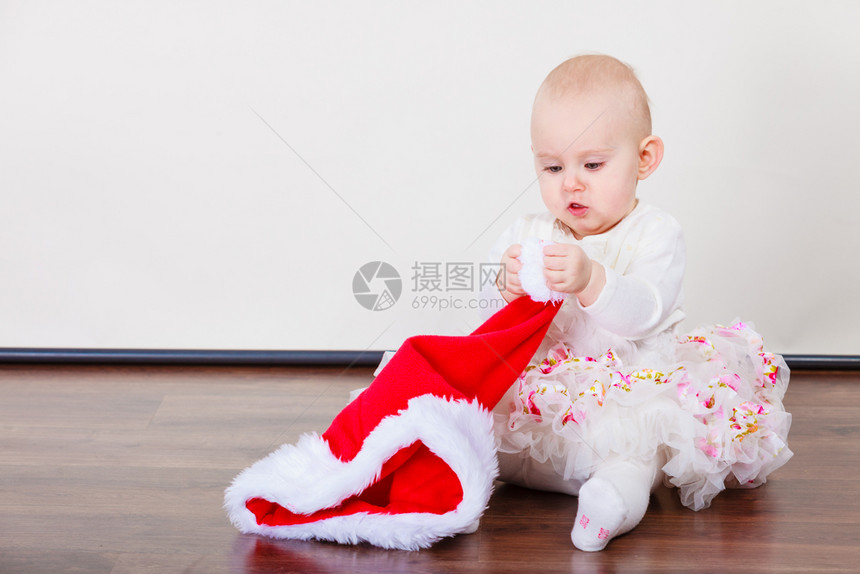 家庭圣诞节人们的概念小女孩坐在地板上可爱的小孩戴着红色的圣坦卡帽子图片
