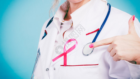 感谢医生战士妇女为健康而斗争乳腺癌肿瘤概念白色医疗围裙制服上的粉色丝带和蓝听诊器医生为疗设备展示制服上的粉色丝带和听诊器背景