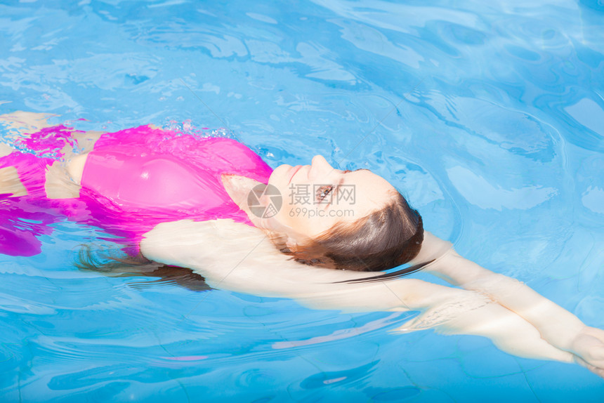 穿着粉红色泳衣在蓝池游的年轻女子在度假胜地游泳的年轻女子体育活动健康概念在游泳池的漂亮女子在游泳池图片