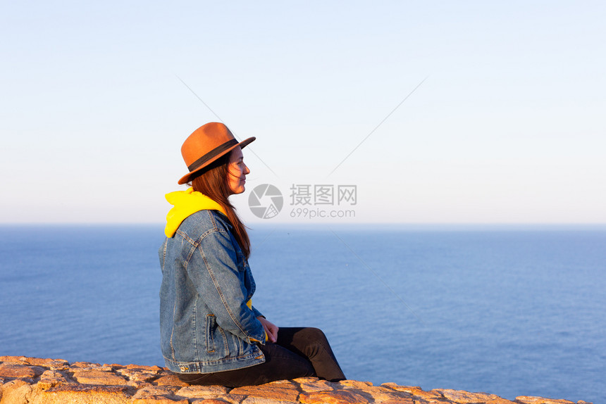 穿旅行服装和戴帽子的妇女坐着看蓝海和天空旅行概念照片坐着和看蓝海天空的妇女图片