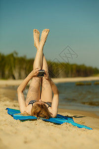 在比基尼日光浴和沙滩上休息的妇女使用智能手机检查社交媒体和写短片在比基尼日光浴和沙滩上休息的妇女背景图片