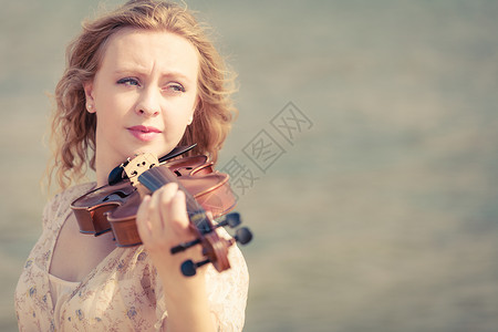 在海边滩上玩小提琴的妇女在沙边小提琴上玩的妇女图片