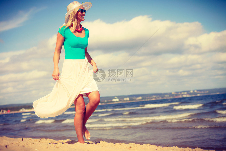 穿着长的浪漫服装迷人金发女子在沙滩上散步和夏天放松图片