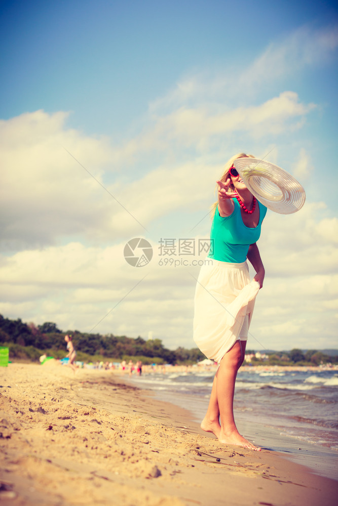 穿着长的浪漫礼服迷人金发女子在沙滩上散步夏天玩得开心戴防晒帽图片