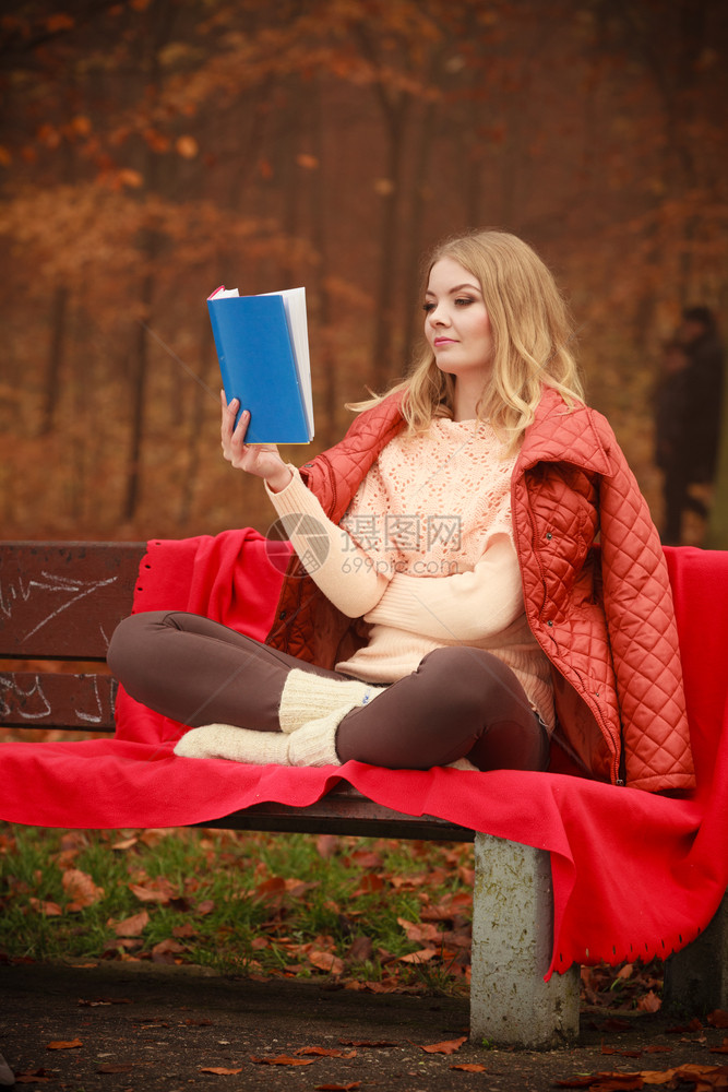 大自然户外休闲文学概念女士阅读蓝皮书秋天森林的金发年轻女孩坐在毯子覆盖的长椅上图片