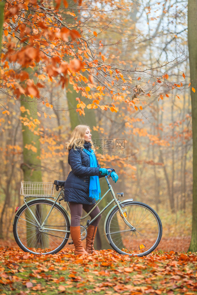年轻女子在户外的秋季公园骑自行车图片