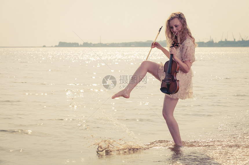 音乐爱好和日常激情概念海边的滩上妇女拿着小提琴在水中玩耍海边的妇女拿着小提琴图片