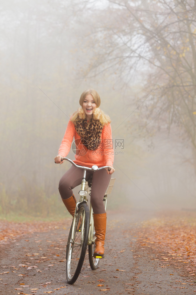 美丽的女子在起雾的公园内骑自行车图片