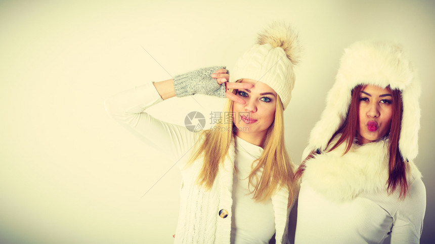 两个穿着温暖白衣的金发女孩和穆拉托玩得开心两个穿着毛帽围巾手套的迷人女两个穿着温暖冬装的女孩玩得开心图片