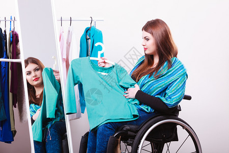 坐在轮椅上的女孩衣柜里选择服或在商店里寻找一些衣服图片