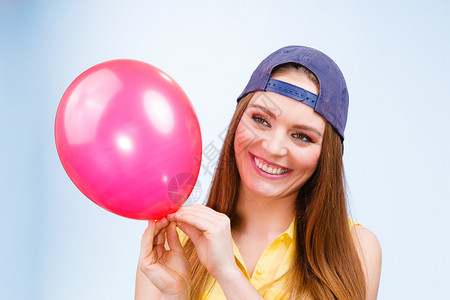 带着红色粉气球的笑容少女穿着时装的年轻迷人时装女郎蓝色背景带着红气球的少女快乐背景图片