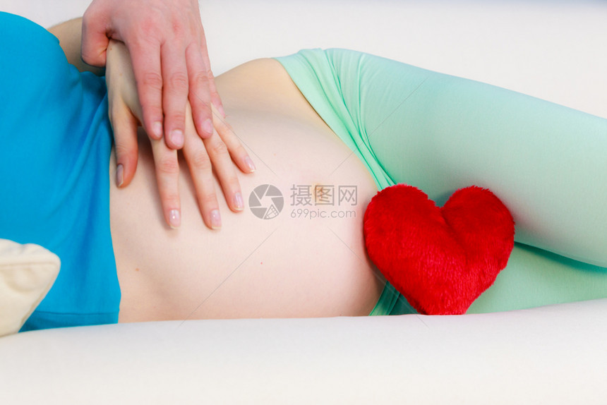 未来母亲躺在沙发上带着红色的心爱符号女人和男的手触摸怀孕肚子做父母的概念图片