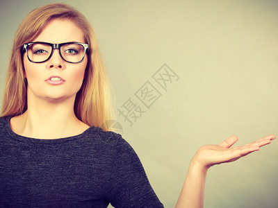 在大眼镜中神经紧张的女人混淆了脸表情用棕榈露的手指着图片