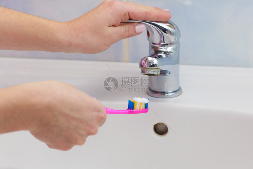 妇女手拿着牙膏刷在浴室水槽和龙头背景中手拿着牙刷在浴室中图片