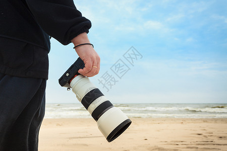 在秋天的气下有闲暇时间在海滩上行走的无法辨认男子持有专业摄影相机图片