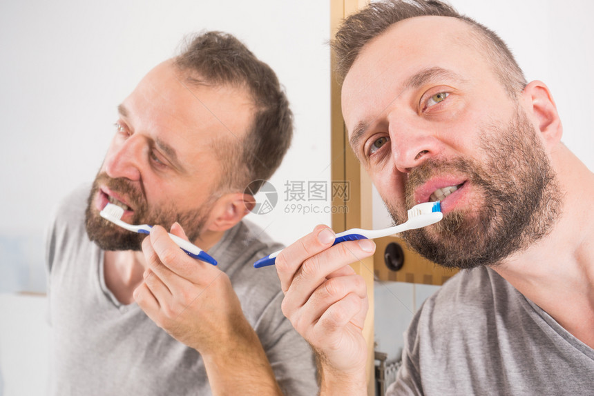 成人男子在清晨卫生例行活动期间在洗手照着浴室镜子刷牙男在洗手间刷牙图片