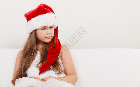 穿着红色圣达克萨斯帽子和白裙的可爱小女孩圣诞节日达克萨斯帽子的小女孩圣诞节背景图片
