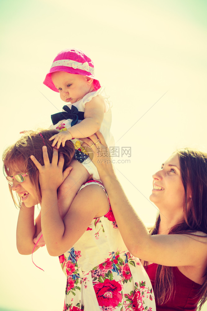 母亲在阳光明媚的日子里穿着夏衣的骑婴儿服装女孩身上抱着和玩儿婴图片