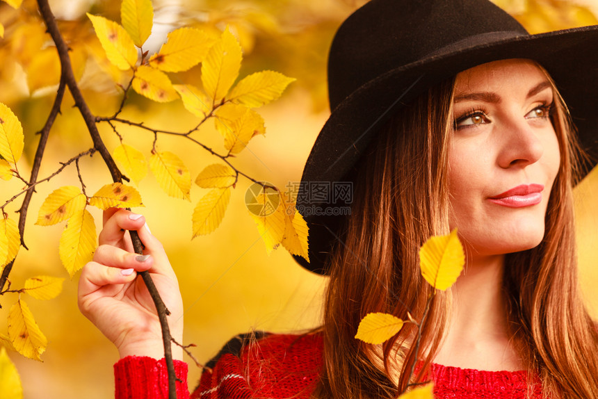 美丽的年轻女子在秋天公园行走时装女孩穿着红色毛衣围巾和黑帽子穿着红色围巾和黑帽子在秋天公园行走的迷人女子在秋天公园行走图片