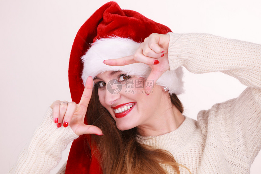 圣诞女孩做手指框的势戴着圣达克莱斯帽子的年轻微笑女士庆祝节日的概念圣诞女人用她的手做架子图片