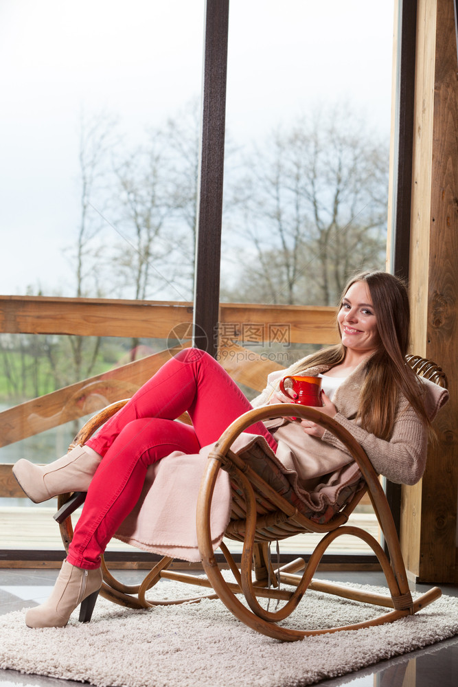 在家里坐摇椅上着舒适的年轻女士坐在摇椅上窗前客厅休息享受咖啡或茶饮图片