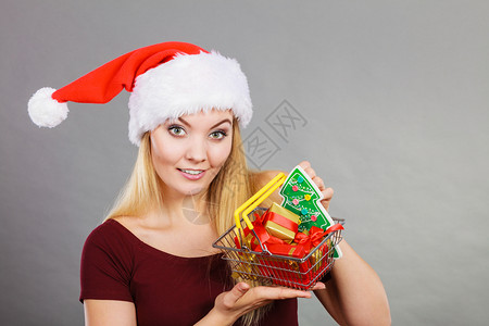 戴圣诞老人帮手帽子的快乐妇女拿着小圣诞树和里面的礼物购篮车背景图片