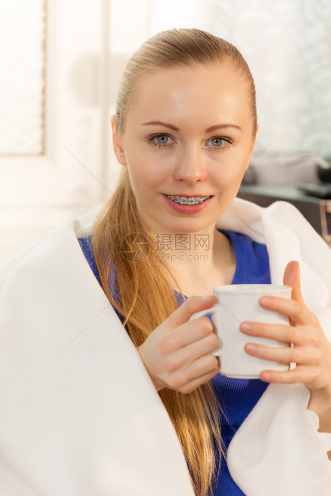 睡在沙发上的年轻女子躺在温暖的毯下喝茶咖啡或不同的热饮图片