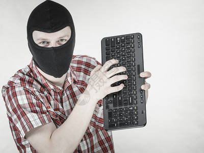 疯狂的黑客男人穿着色的balaclava拿着电脑键盘网上的仇恨言论背景图片