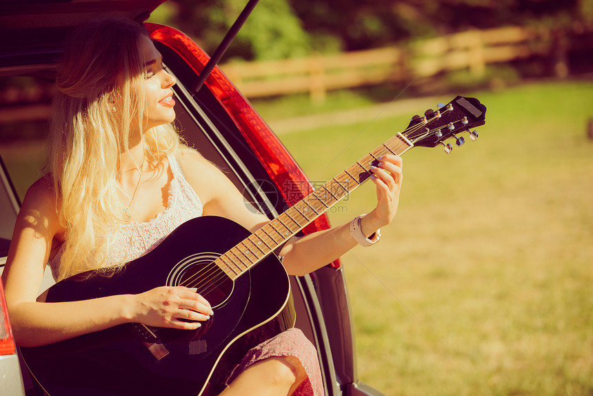 穿长裙的妇女坐在露营面包车里手持吉他图片