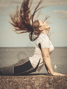 穿着时尚服装的漂亮年轻女子在外面积极工作在海边练瑜伽有风吹的头发图片