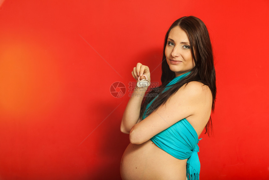 成年妇女展示她的大肚子怀着奶嘴红背景的室内成年妇女展示她的怀孕肚子图片