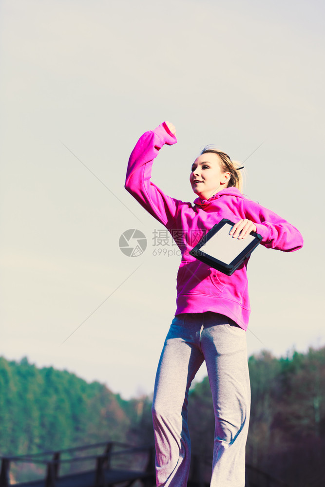 年轻女孩在公园里用平板电脑跳跃的火车锻炼以保持体型注意健康的生活方式和微弱的身材快乐感觉女孩在公园里跳跃图片