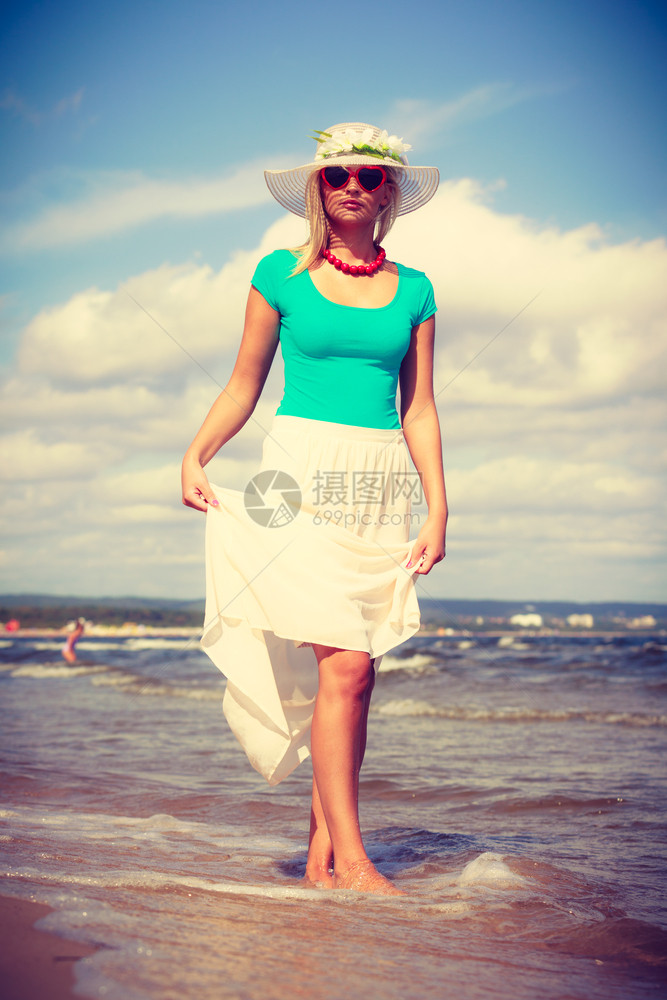 穿着长的浪漫服装迷人金发女子在沙滩上散步和夏天放松图片