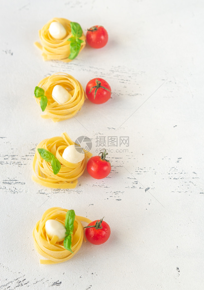 Rawfettucnune配有马扎里拉球樱桃西红柿和白色背景的新鲜叶图片