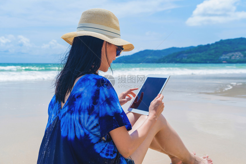 在泰国普吉中午的海洋或自然户外旅行度假时快乐的亚洲妇女在海滩使用一块平板图片