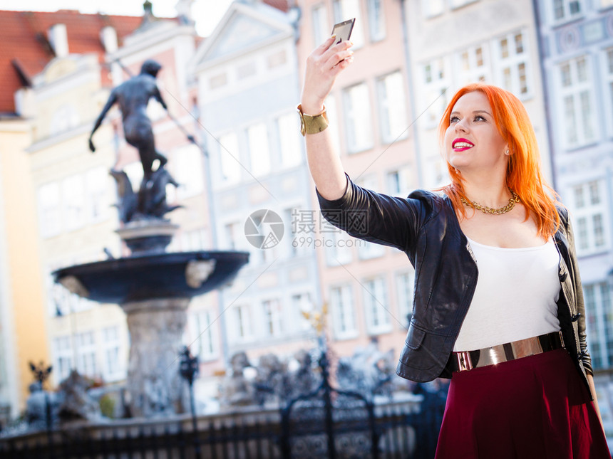 穿红发女旅行者头时装女郎拍摄自己智能手机相在欧佩安市老城格但斯克户外拍摄图片