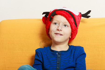 坐在沙发上的小男孩戴着红色的圣诞帽子和角在沙发上的小男孩戴着圣诞帽子图片