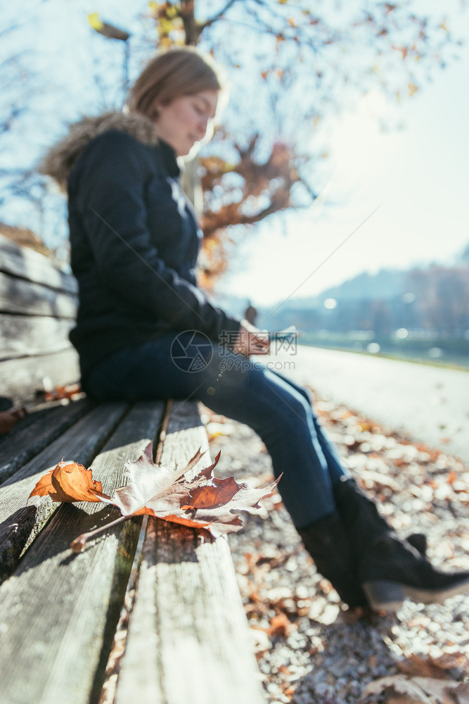 秋天的公园长凳女人坐在它上模糊的背景图片