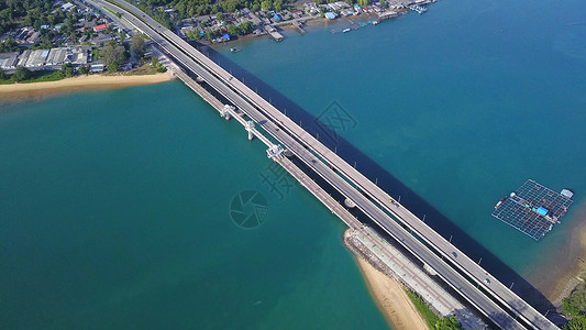 在泰国普吉湾岛安达曼海岸湾岛沙滩热带海和浪在夏季滚入岸的天然林树热带海滩和浪的桥船上驾驶汽车的空中景象图片