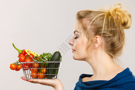 有吸引力的妇女拿着购物篮里面有绿色的红蔬菜闭着眼睛闻建议用灰色的健康高纤维饮食有吸引力的妇女拿着蔬菜有嗅觉背景