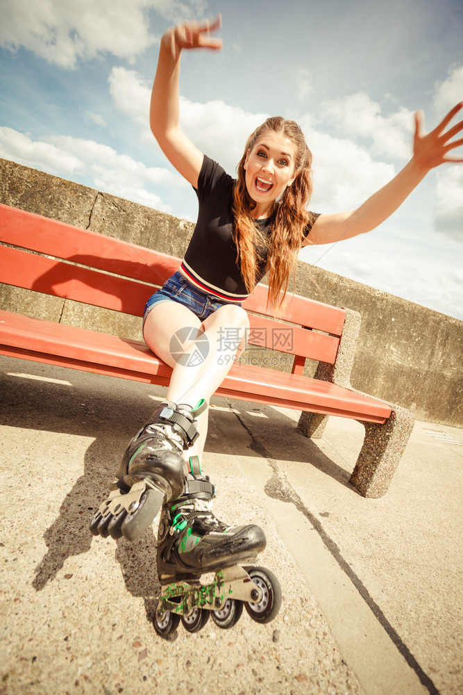 快乐的年轻女子穿着滑冰鞋坐在长凳上享受快乐女在夏季玩得愉快年轻女子骑滑冰图片